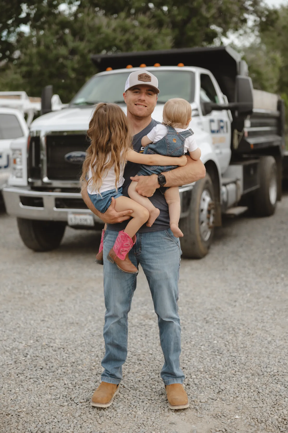 CJR owner Colton Ray holding his two children in front of a CJR dump truck