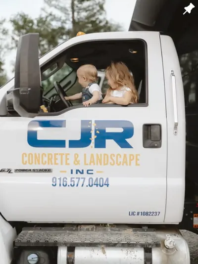 Two young children sitting in the cab of a white CJR Concrete & Landscape work truck