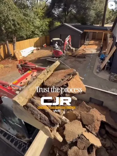 Excavator bucket lifting broken concrete during demolition of a backyard, mini excavator in the background