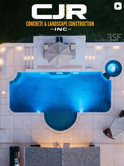 Drone view at dusk of a lit rectangular pool with spa, umbrella, and concrete deck