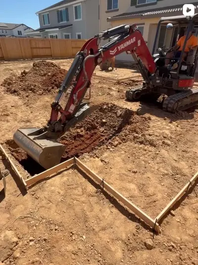 Red Yanmar mini excavator digging inside wood form boards for a new backyard project