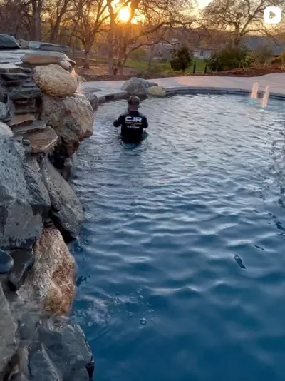 CJR crew member wading in a new freeform pool below a rock waterfall at sunrise