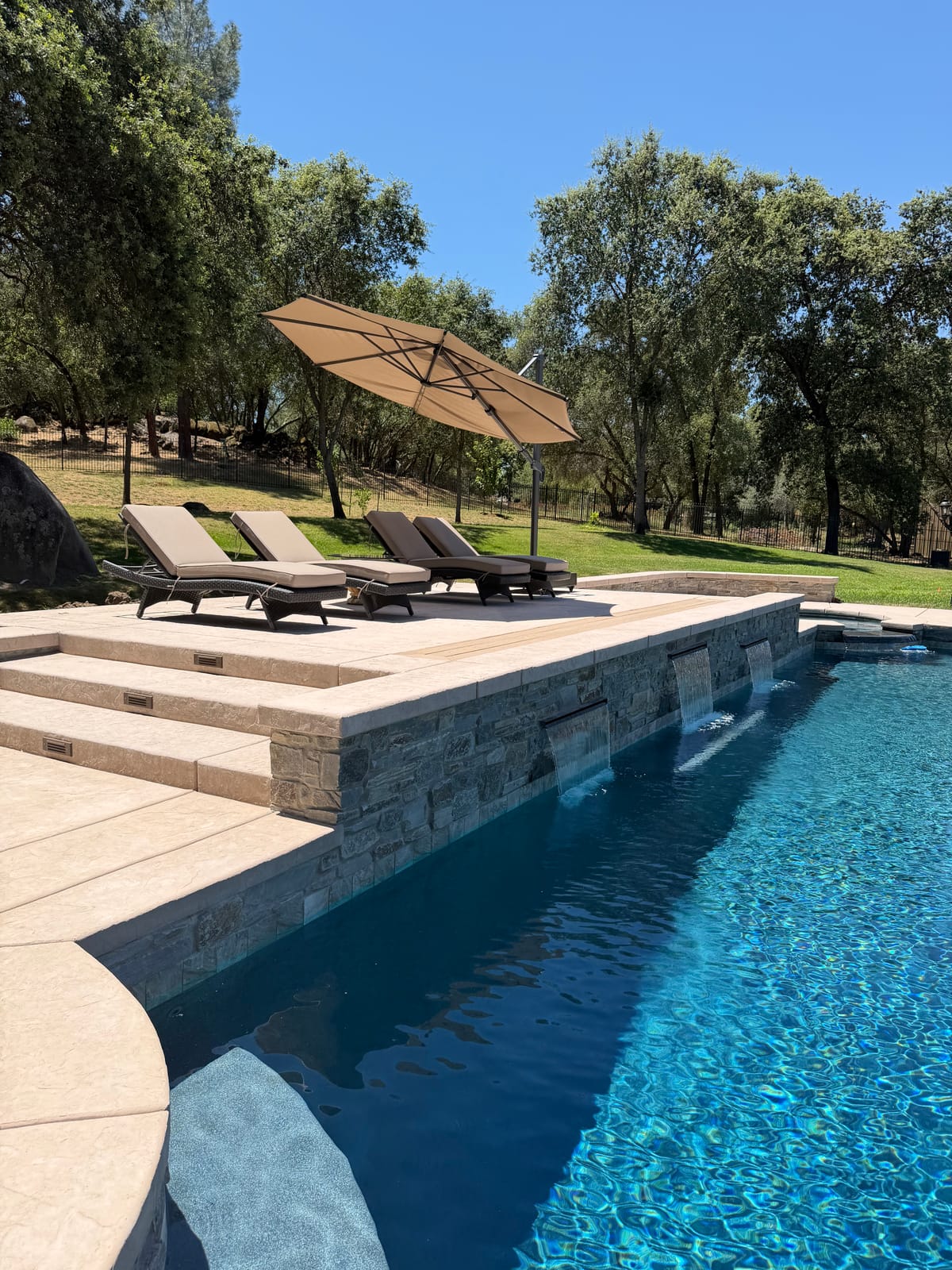 Custom CJR pool with raised stacked-stone wall, sheer descents, umbrella and loungers